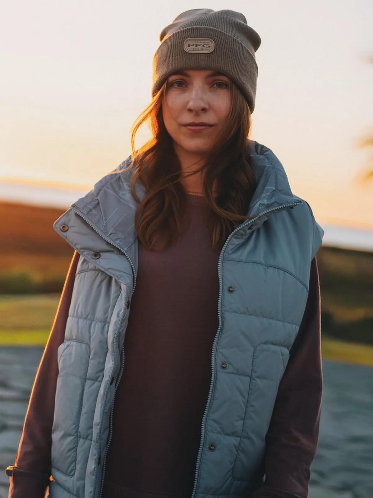 Woman in a Columbia vest and beanie on open water at sunset