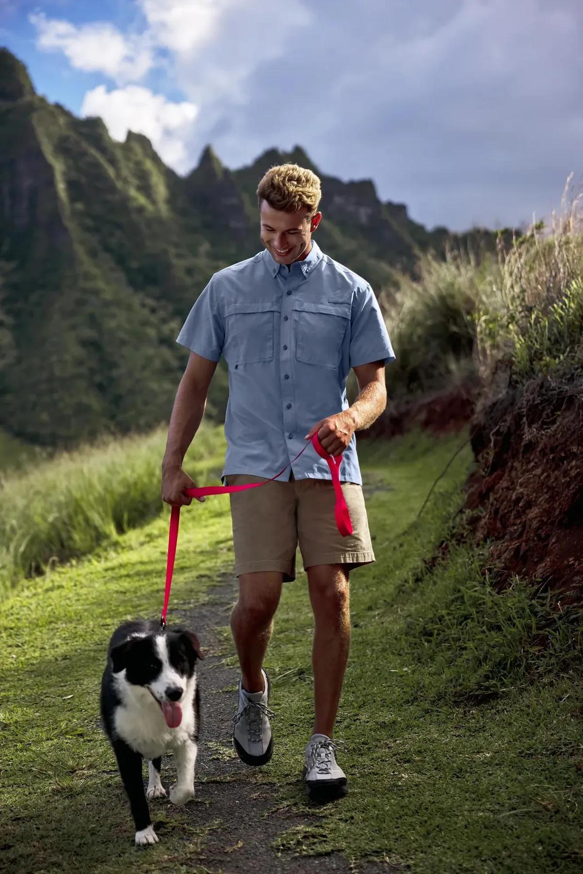 Man in an Eddie Bauer ripstop shirt hiking a trail with a dog