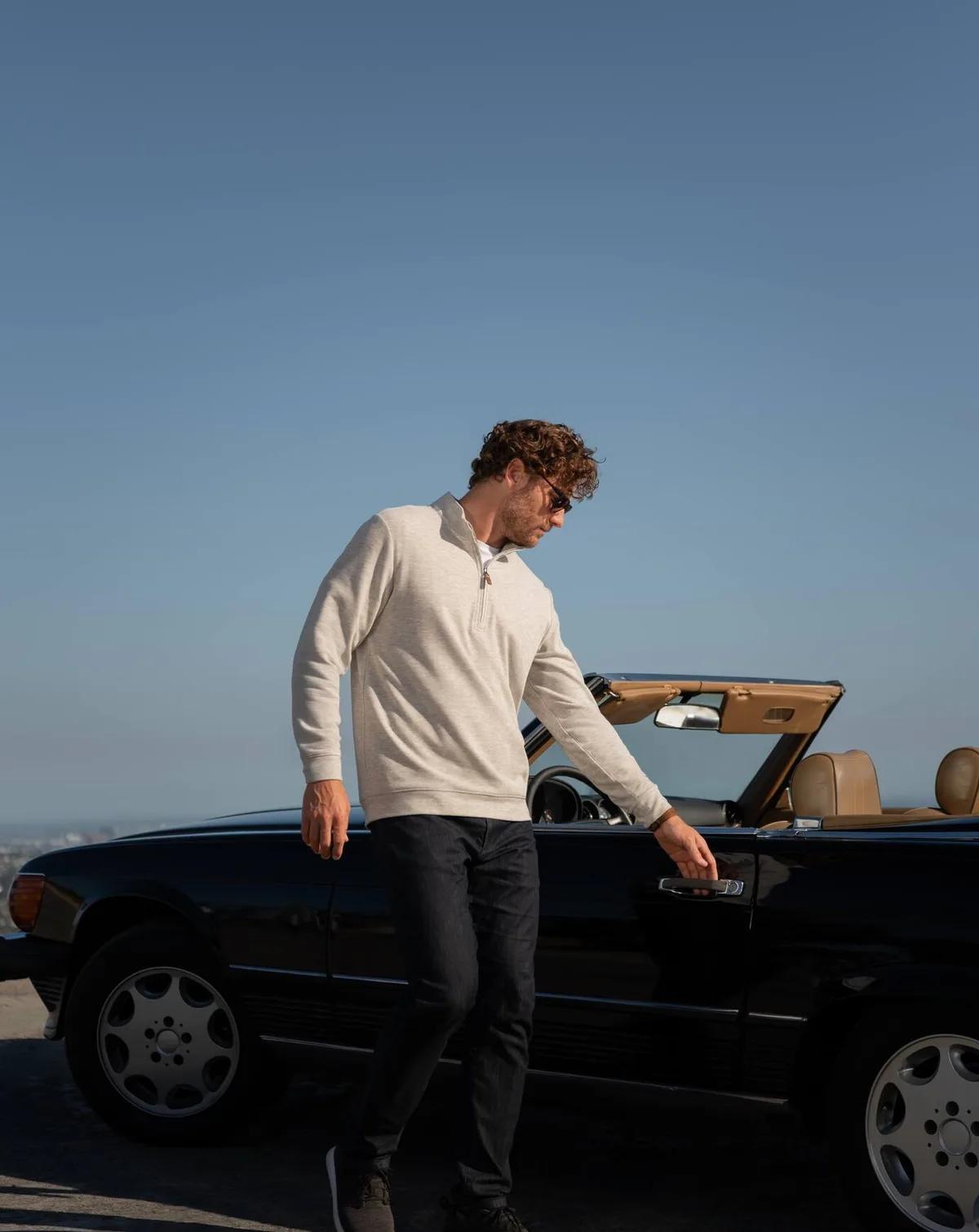 Man in a cream TravisMathew quarter-zip beside a convertible